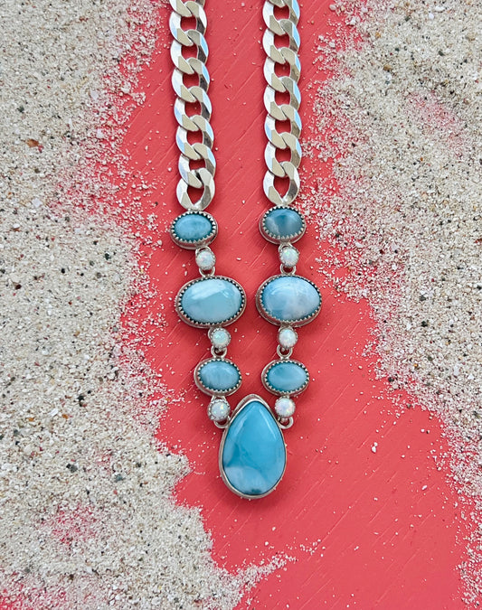 Necklace with blue teardrop pendants and silver chain on a textured surface