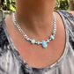 Necklace with blue stones and silver chain worn by a person, with a blurred outdoor background.