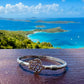 Silver bracelet with a unique design on a wooden surface with a scenic ocean view in the background.