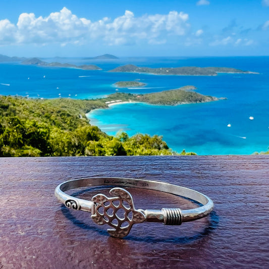 Silver bracelet with a unique design on a wooden surface with a scenic ocean view in the background.