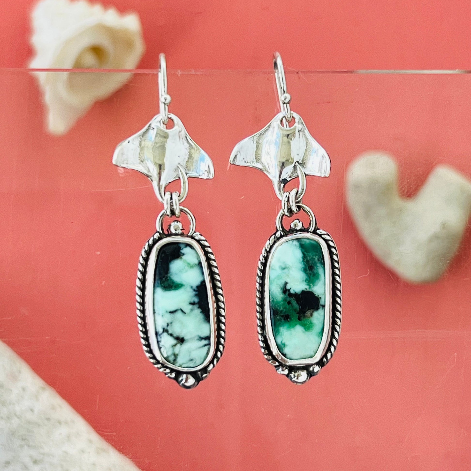 Silver earrings with green stone drops on a pink background