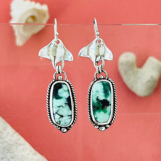 Silver earrings with green stone drops on a pink background