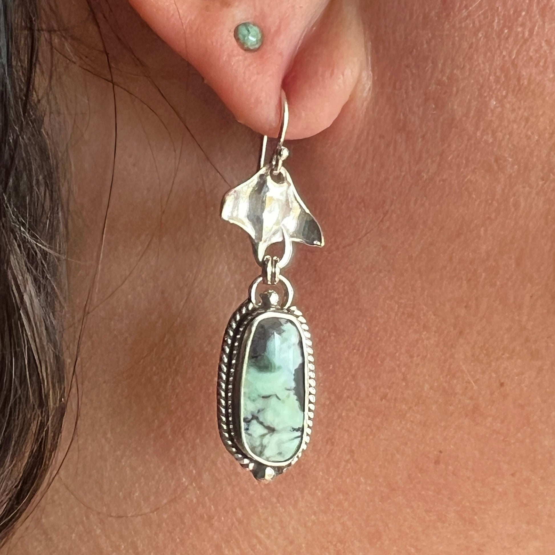 Close-up of a silver earring with a turquoise stone worn on an ear.