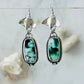 Silver earrings with green gemstones on a light gray background