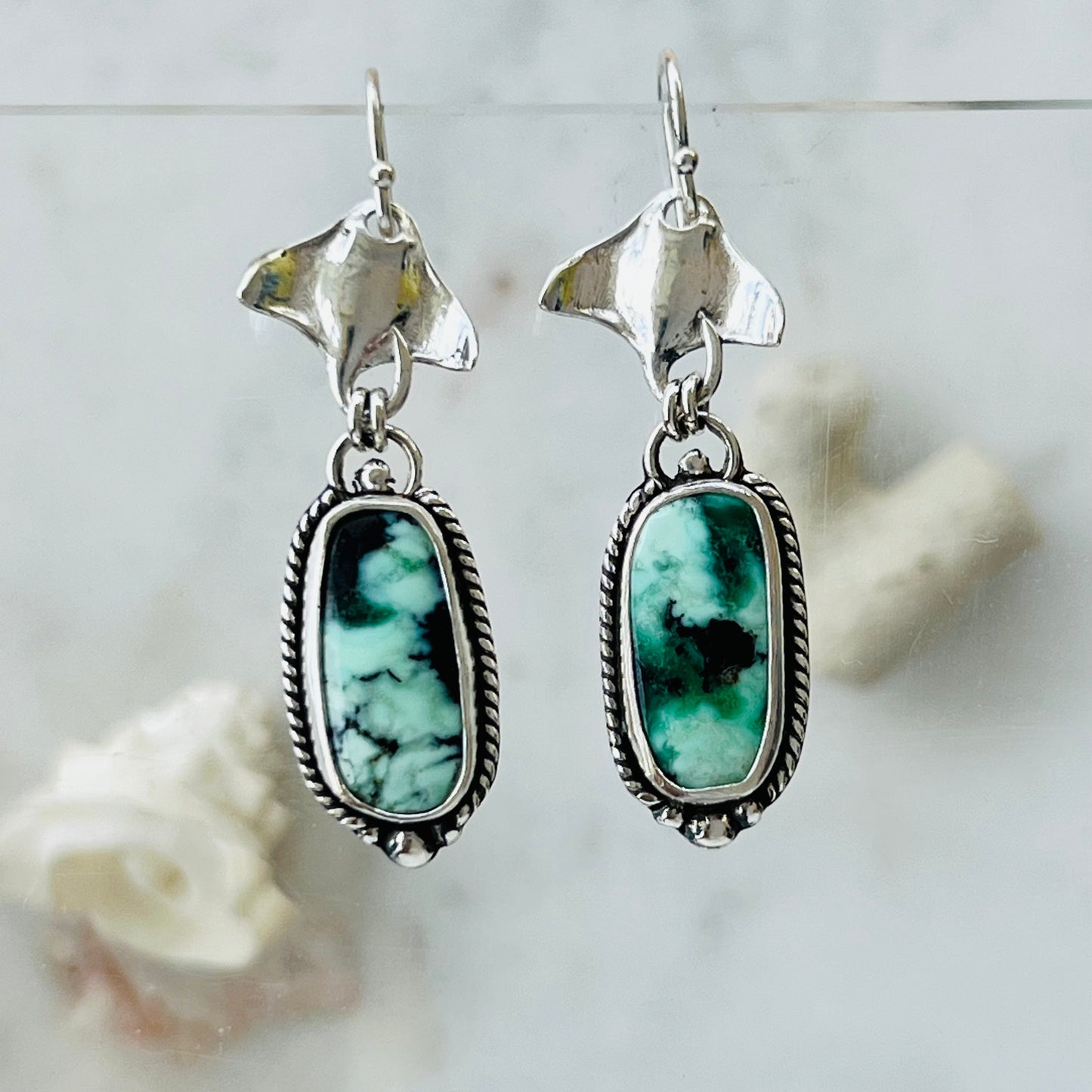 Silver earrings with green gemstones on a light gray background