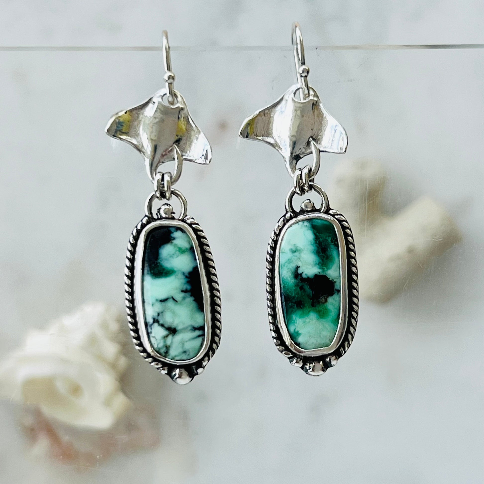 Silver earrings with green gemstones on a light gray background