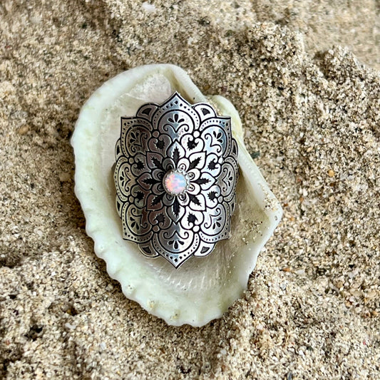 Decorative silver mandala on a white shell in sand