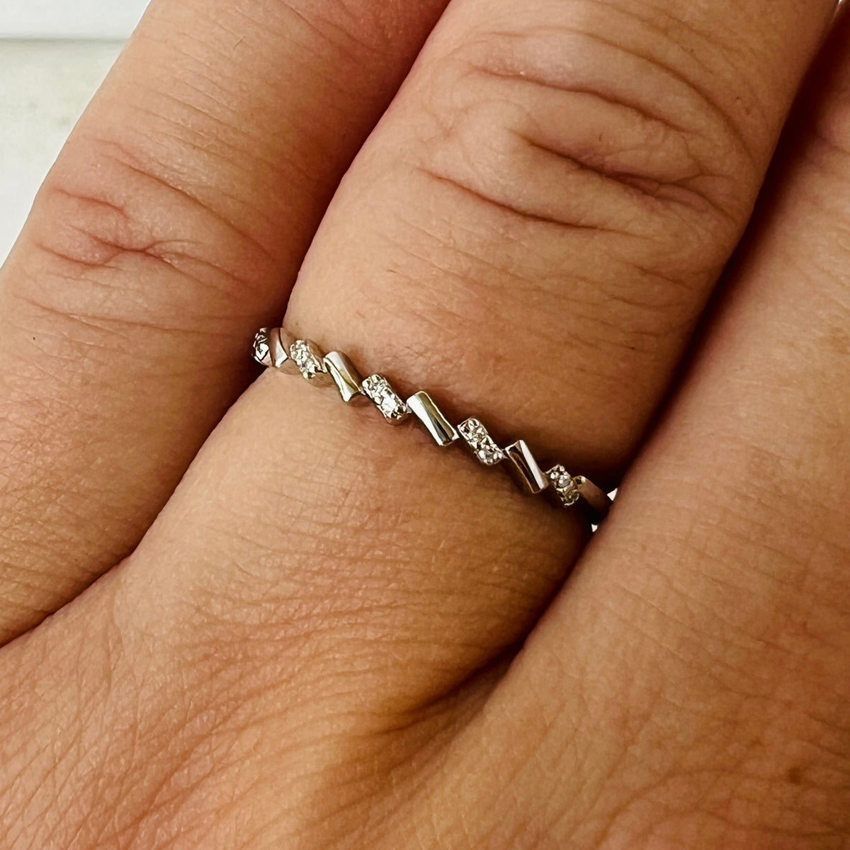 A close-up of a silver ring with small diamond stones set in a chevron pattern, worn on a finger.