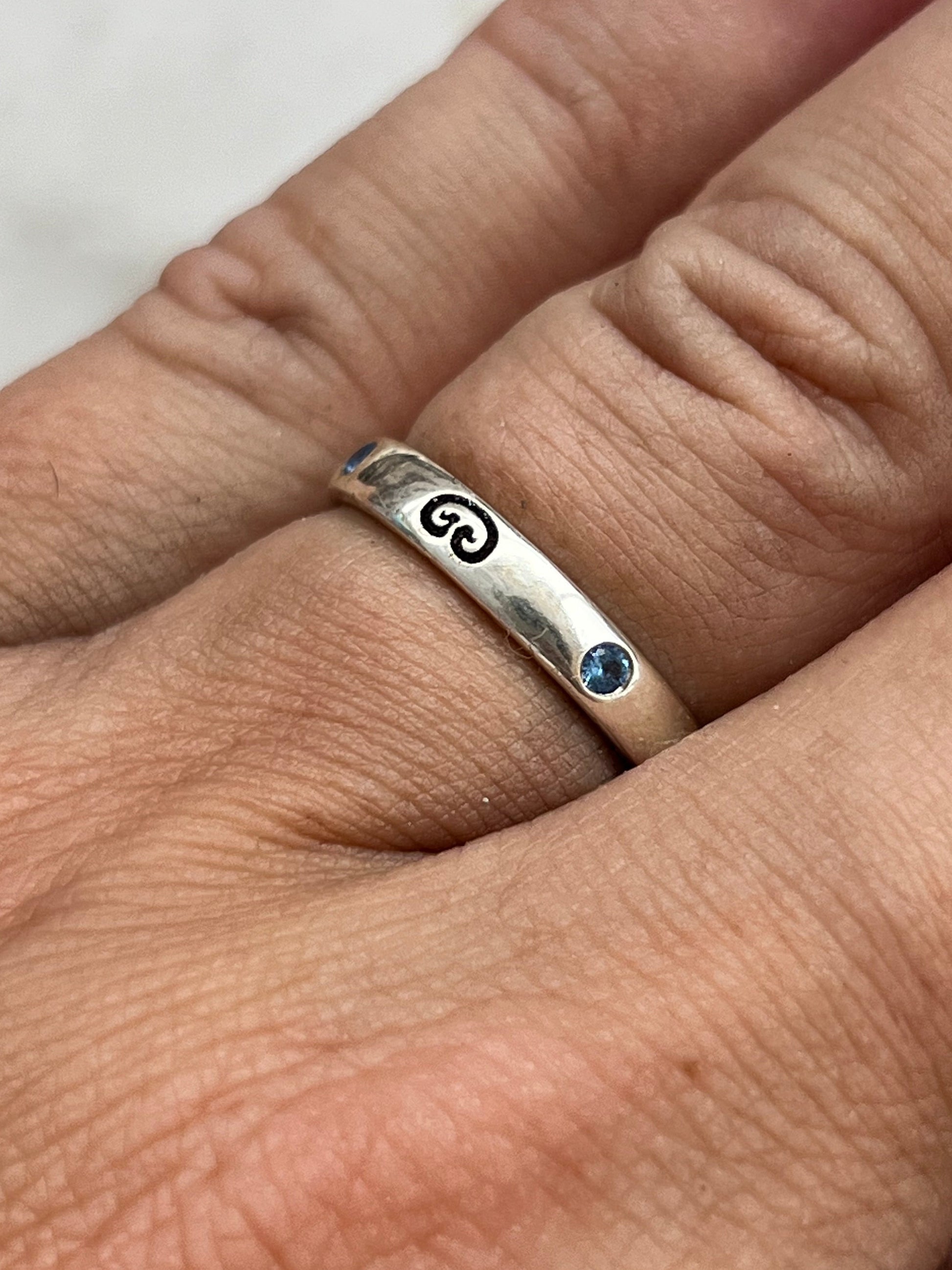 Silver ring with a blue gemstone on a finger against a white background