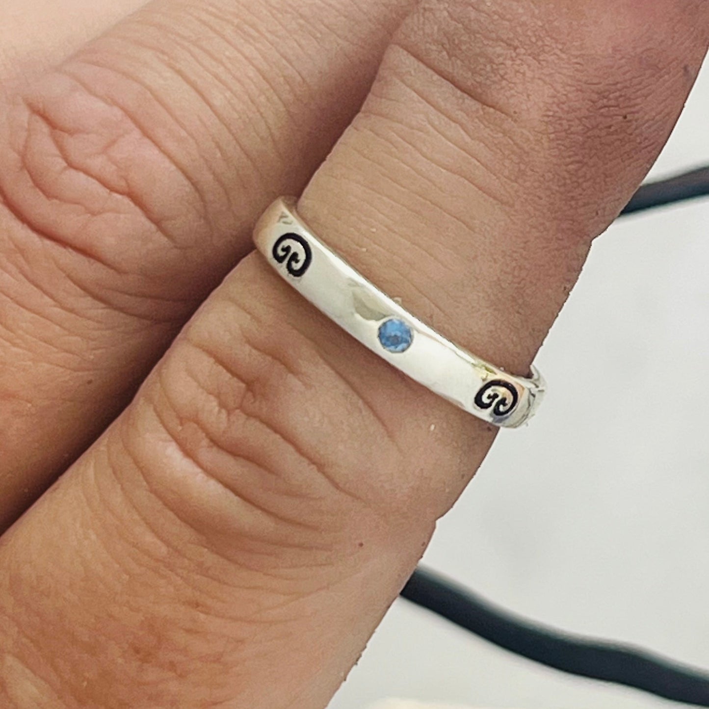 Silver ring with a blue gemstone on a finger against a neutral background