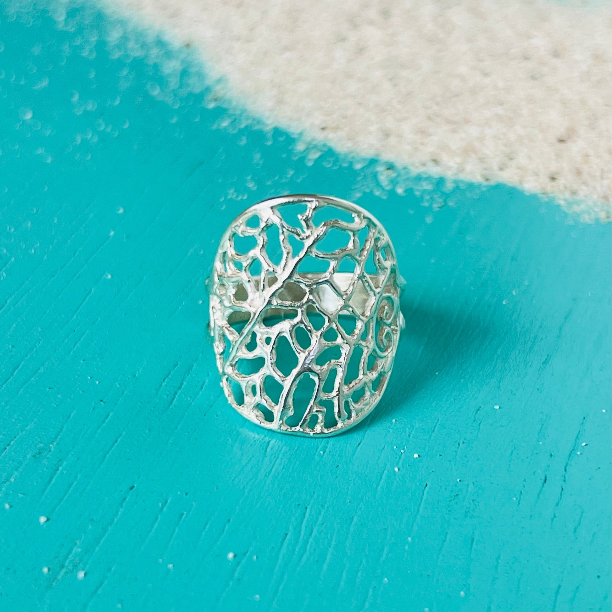 Silver ring with intricate design on a turquoise surface
