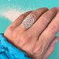 Hand wearing a silver lace ring against a turquoise background