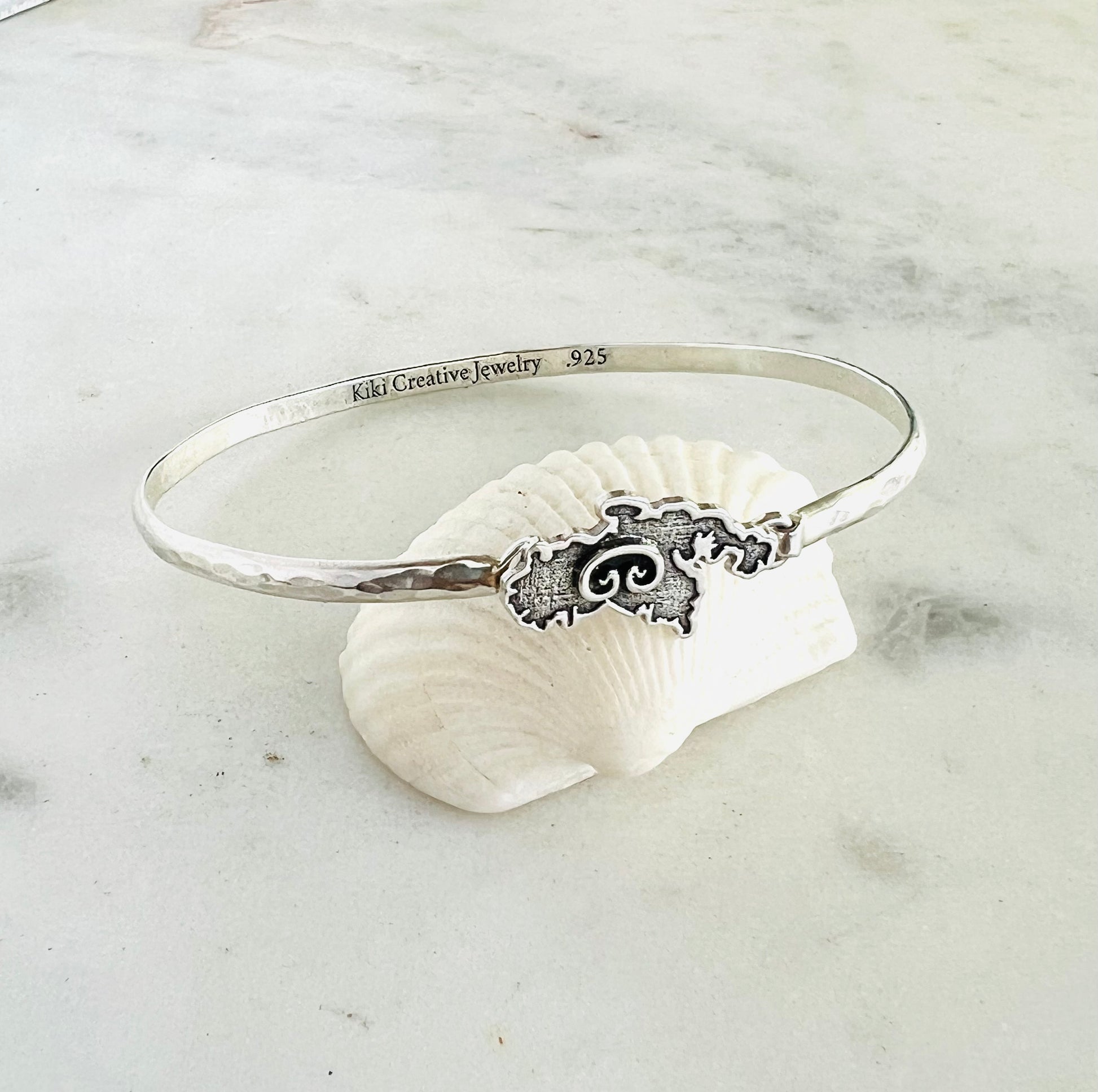 Silver bracelet with shell design on a white shell against a marble background