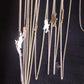 A close-up of several silver-toned chain necklaces with small animal-shaped pendants hanging against a black background.