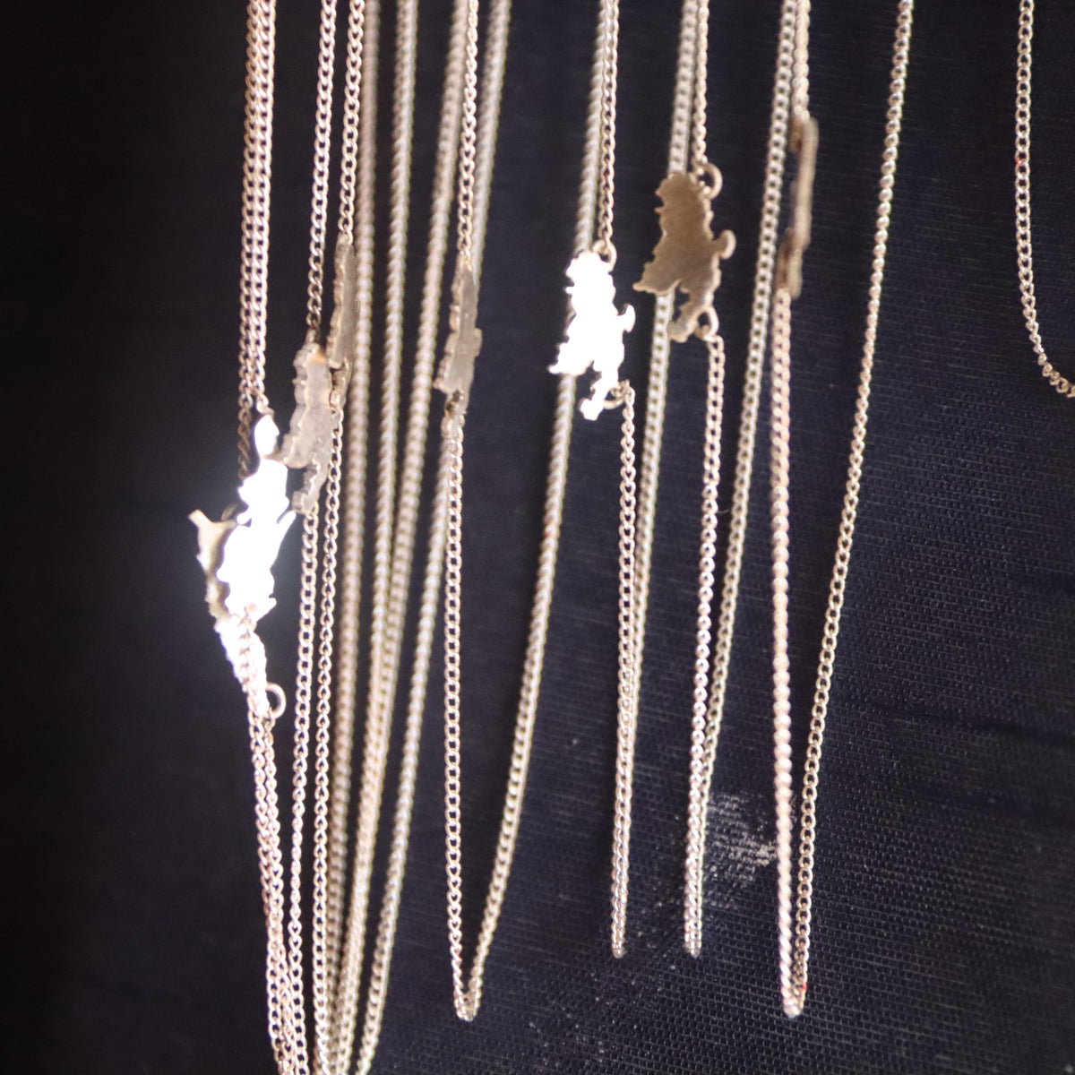 A close-up of several silver-toned chain necklaces with small animal-shaped pendants hanging against a black background.