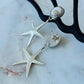 Silver starfish earrings on a marble surface with a black metal stand.