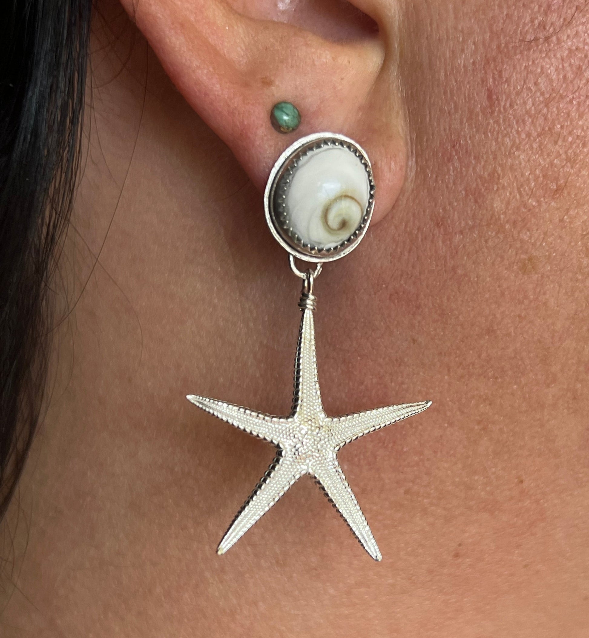 Silver starfish earring worn on a person's ear