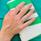 Hand holding a green and white clutch with a decorative ring on a teal wooden surface