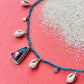 Necklace with shell and gemstone charms on a pink and white gradient background
