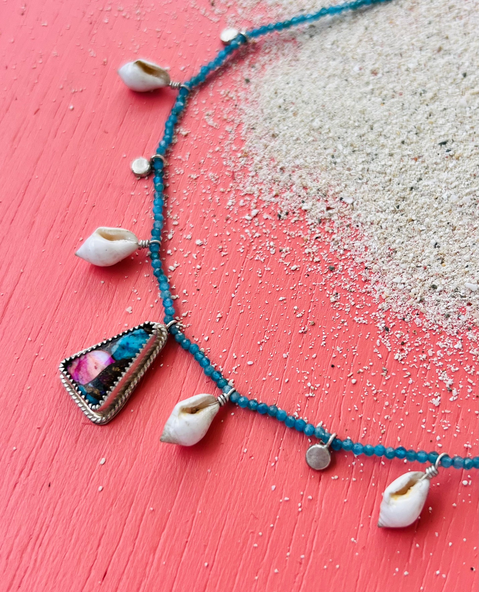 Necklace with shell and gemstone charms on a pink and white gradient background