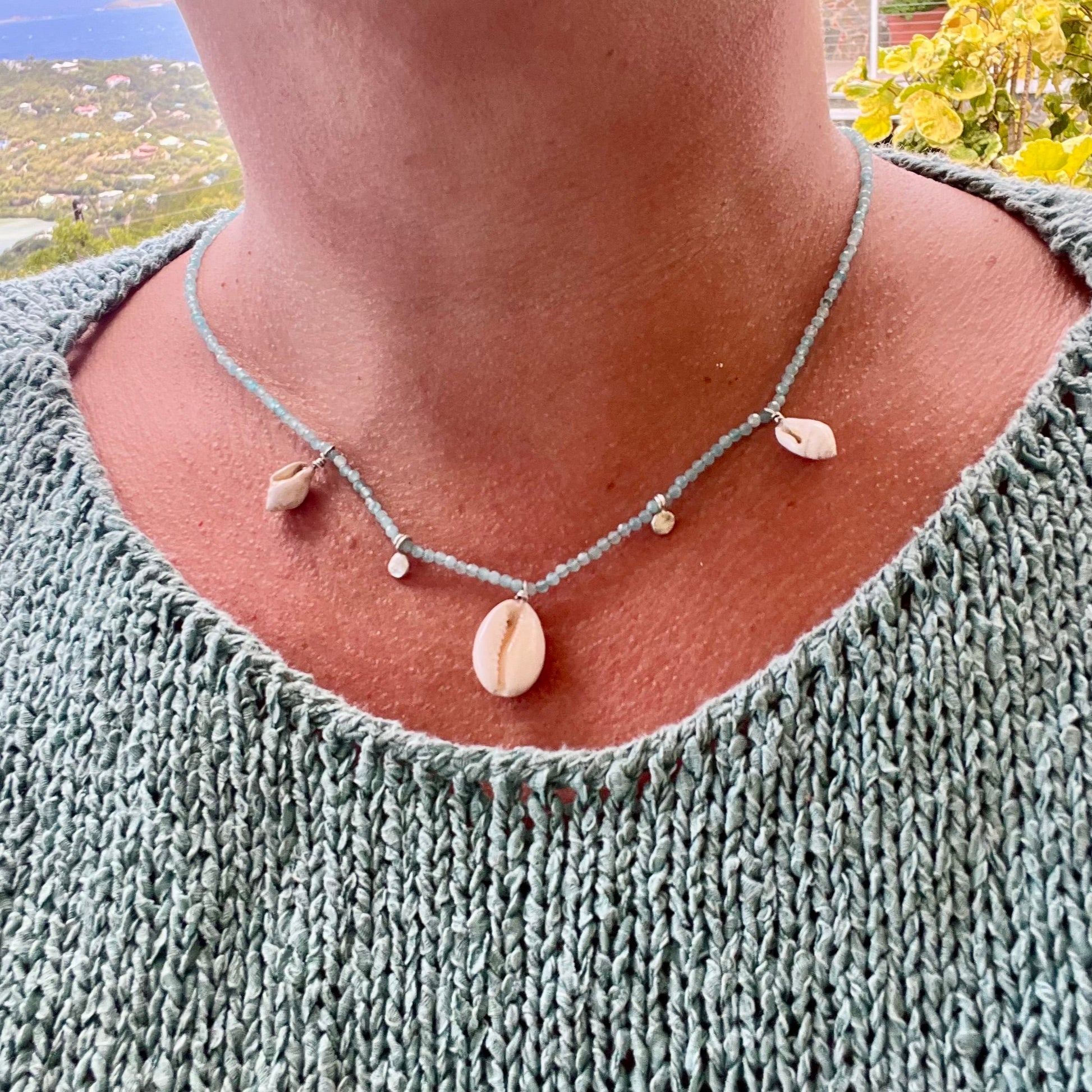 Necklace with shell pendants worn by a person in a green sweater outdoors.