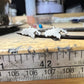 Two small silver-colored earring pieces held on forceps above a metal ruler on a wooden workbench.