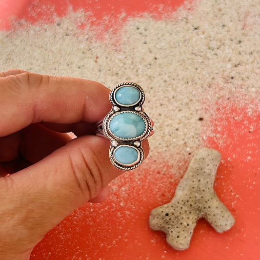 Hand holding a silver ring with blue stones on a sandy surface