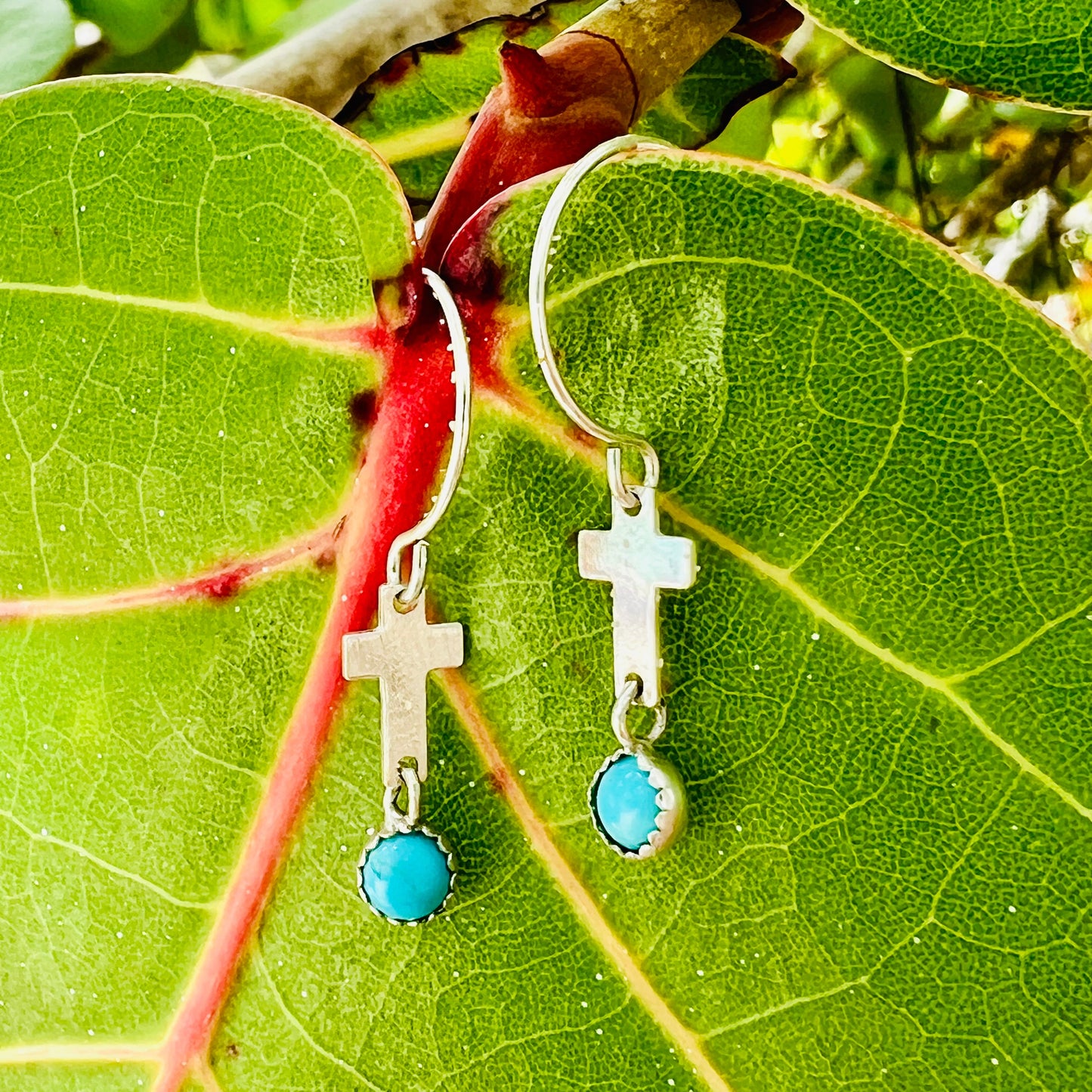 Silver earrings with turquoise stones on a green leaf