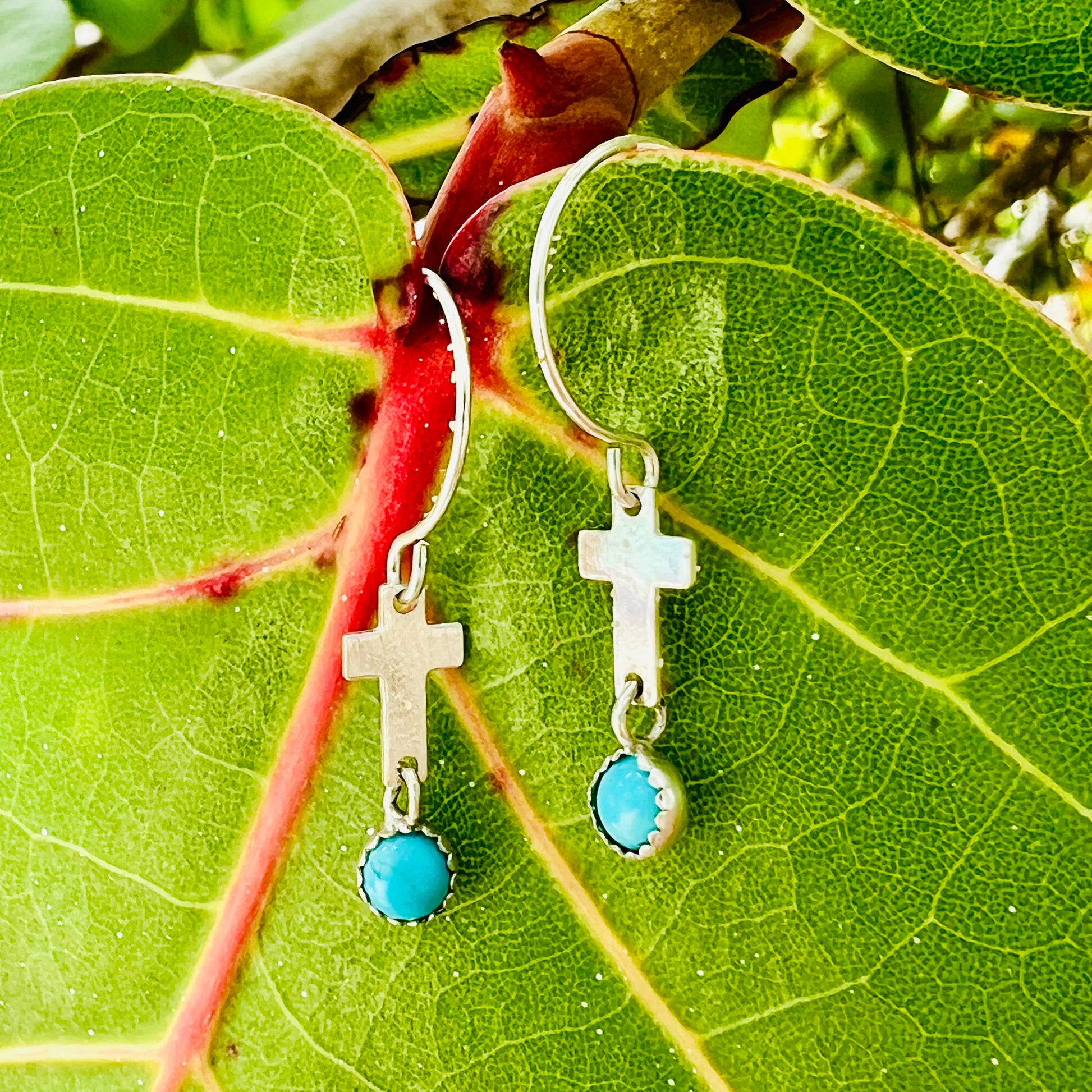 Silver earrings with turquoise stones on a green leaf