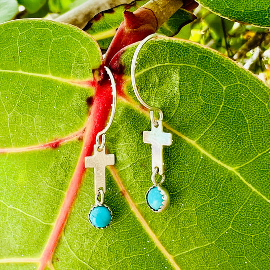 Silver earrings with turquoise stones on a green leaf