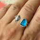 Hand wearing two rings: a silver turtle-shaped ring and a blue stone ring.