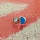 Silver turtle charm and blue sea glass ring on a sandy surface