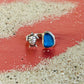 Ring with blue stone and turtle charm on a sandy surface